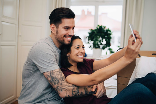 Happy couple taking selfie on mobile phone while resting in bedroom
