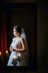 Fototapeta na wymiar Thoughtful bride stands before a window in dark room with candles