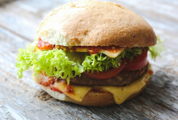 Tasty homemade cheeseburger with mustard, tomatoes and green lettuce. Sesame burgers on wooden background. Food photo.