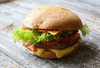 Tasty homemade cheeseburger with mustard, tomatoes and green lettuce. Sesame burgers on wooden background. Food photo.