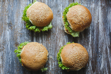 Tasty homemade cheeseburger with mustard, tomatoes and green lettuce. Sesame burgers on wooden background. Food photo.