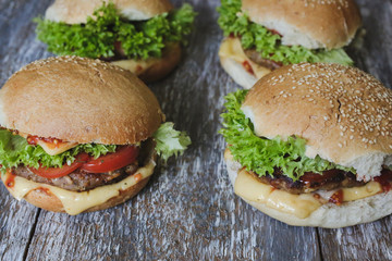Tasty homemade cheeseburger with mustard, tomatoes and green lettuce. Sesame burgers on wooden background. Food photo.
