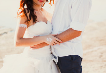 Wedding couple hugs on the sea beach. Sunny summer photo. Bride with hair down in off shoulder...
