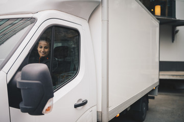 Smiling female worker driving white delivery van in city