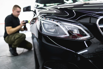 Fototapeta premium Car detailing - Worker with orbital polisher in auto repair shop. Selective focus.