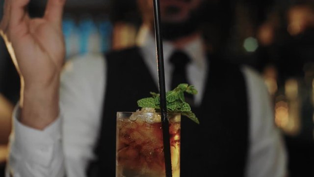 Professional bartender at bar, twists lemon peel to add flavor and itric touch to cocktail, after pouring dark and stormy rum and ginger beer drink into highball glass, decorated with mint