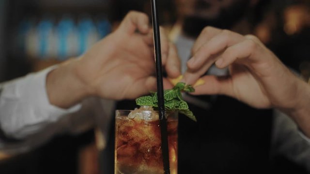 Professional bartender at bar, twists lemon peel to add flavor and itric touch to cocktail, after pouring dark and stormy rum and ginger beer drink into highball glass, decorated with mint