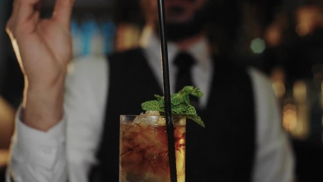 Professional bartender adds finishing touches to fancy and exquisite long drink, mojito or dark and stormy cocktail, with mint and ginger ale. Adds twist of lemon fragrance