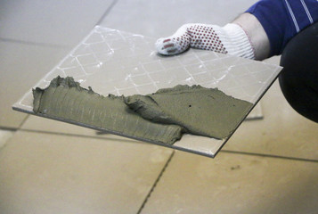 Repair - interior decoration. Laying of floor ceramic tiles. Men's hands tiler in gloves with  spatula spread  cement mortar on  ceramic floor tile.