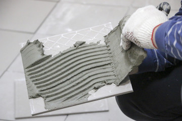 Repair - interior decoration. Laying of floor ceramic tiles. Men's hands tiler in gloves with  spatula spread  cement mortar on  ceramic floor tile.