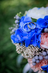 Obraz na płótnie Canvas Golden wedding rings lie on blue bouquet for a bride