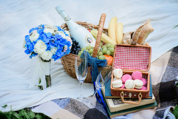 Little box with colorful macaroons stands on the books on the blanket with wedding bouquet and bottle of champagne