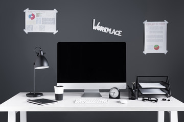 desktop computer with blank screen, business charts and office supplies at workplace