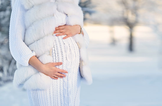 Happy Pregnant Woman Waiting For Baby In Winter. Pregnant Woman Holding Her Belly In Winter Park. Pregnancy Concept. Future Mom Walking In Park And Breathing Fresh Air. Portrait Of Expectant Mother