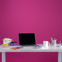 laptop with blank screen, doughnut with coffee, camera, cosmetics and office supplies on pink