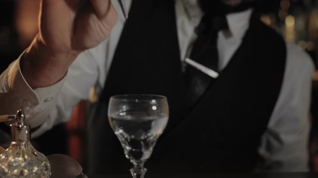 Professional bartender at expensive and luxurious unique bar, prepares fancy drink or cocktail, dry martini in vintage glass, uses infusions or insense to add flavor