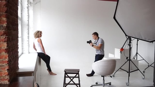 Photographer takes a picture near the window for a young model in the studio