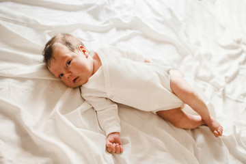 Newborn baby lies on white bed in a bright room