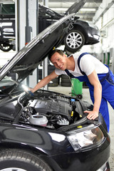 freundlicher KFZ Mechaniker untersucht Motor eines Autos in einer Werkstatt // friendly car repair...