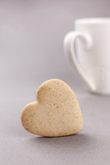 cookies in the shape of a heart on a gray background and a white cup in the background, minimalism, a concept of cooking, baking, a symbol of love