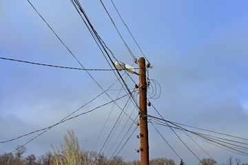 Wooden electric pole with wires on the street in the city against a blue sky.