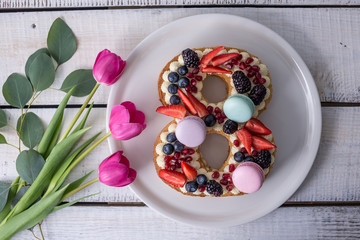 Cake in shape of number 8 decorated with berries and flowers tulips. Dessert for women's day on the eighth of March