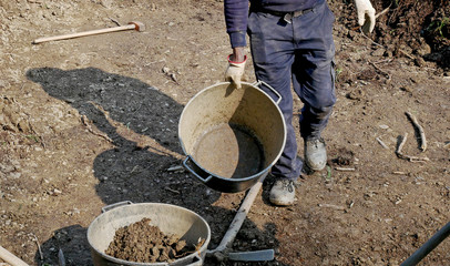 Man at work with shovel, pick and bucket on a rough ground to cultivate. 