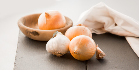 Bowl with onions and garlic with tablecloth on dark background, 