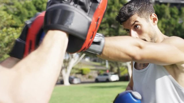 Young athletic male doing boxing training outdoors in a park, in slow motion