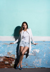 Fototapeta na wymiar The style and fashion. Portrait in full growth, beautiful young woman near a bright wall color. Long white sweater and short denim shorts