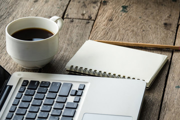 Top view of blank notebook with white coffee, laptop and with natural light on wooden table.