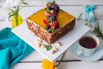 Homemade square cake decorated on top of yellow jelly and berries with mint on light background.
