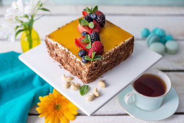Homemade square cake decorated on top of yellow jelly and berries with mint on light background.