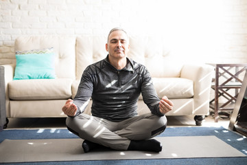 Mature man meditating in lotus pose at home