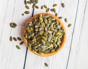 Bowl with raw pumpkin seeds on wooden background