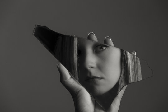 Woman looking at her face in a shard of broken mirror artistic conversion