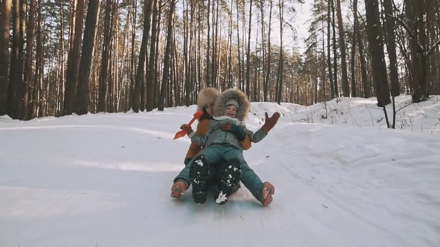 Young mother and little daughter having fun on sledge in winter park. Steadicam shot. Cold snowy weather. Active leisure concept.