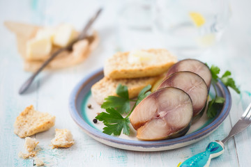Smoked mackerel or cured mackerel slices on a plate with fresh parsley and bread