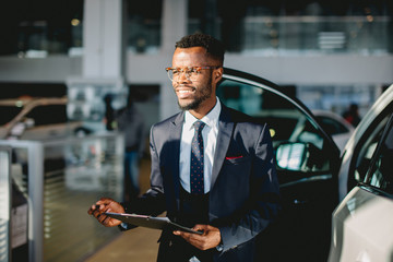 Handsome young african car salesman standing at the dealership holding a tablet