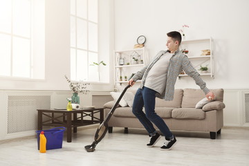 Young man cleaning home, playing with vacuum cleaner