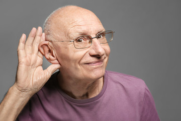 Elderly man with hearing problem on grey background