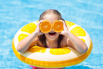 Child in swimming pool. Kid eating orange.