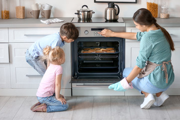 Little kids watching their mother bake cookies in oven indoors