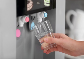 Woman filling glass from water cooler, closeup