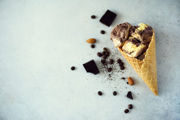 Chocolate, vanilla and coffee ice cream in waffle cone with coffee beans on grey stone background. Summer food concept, copy space. Healthy gluten free ice-cream