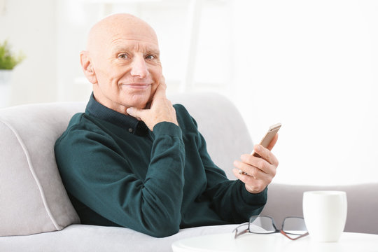Senior man with hearing aid using smartphone indoors