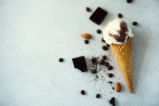Chocolate, vanilla and coffee ice cream in waffle cone with coffee beans on grey stone background. Summer food concept, copy space. Healthy gluten free ice-cream