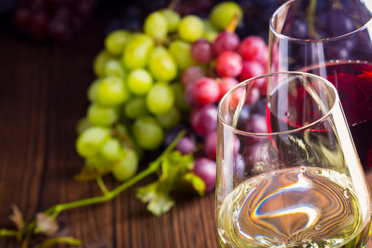 Close-up of glasses with red and white wine with grapes on wooden background 