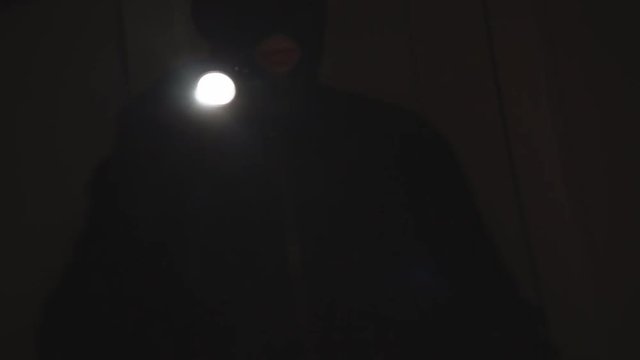 Thief with a flashlight walking inside apartment at night.