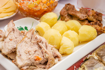 Two kinds of fried and baked meat lying diagonally on a white dish young boiled potatoes in the center of a hill